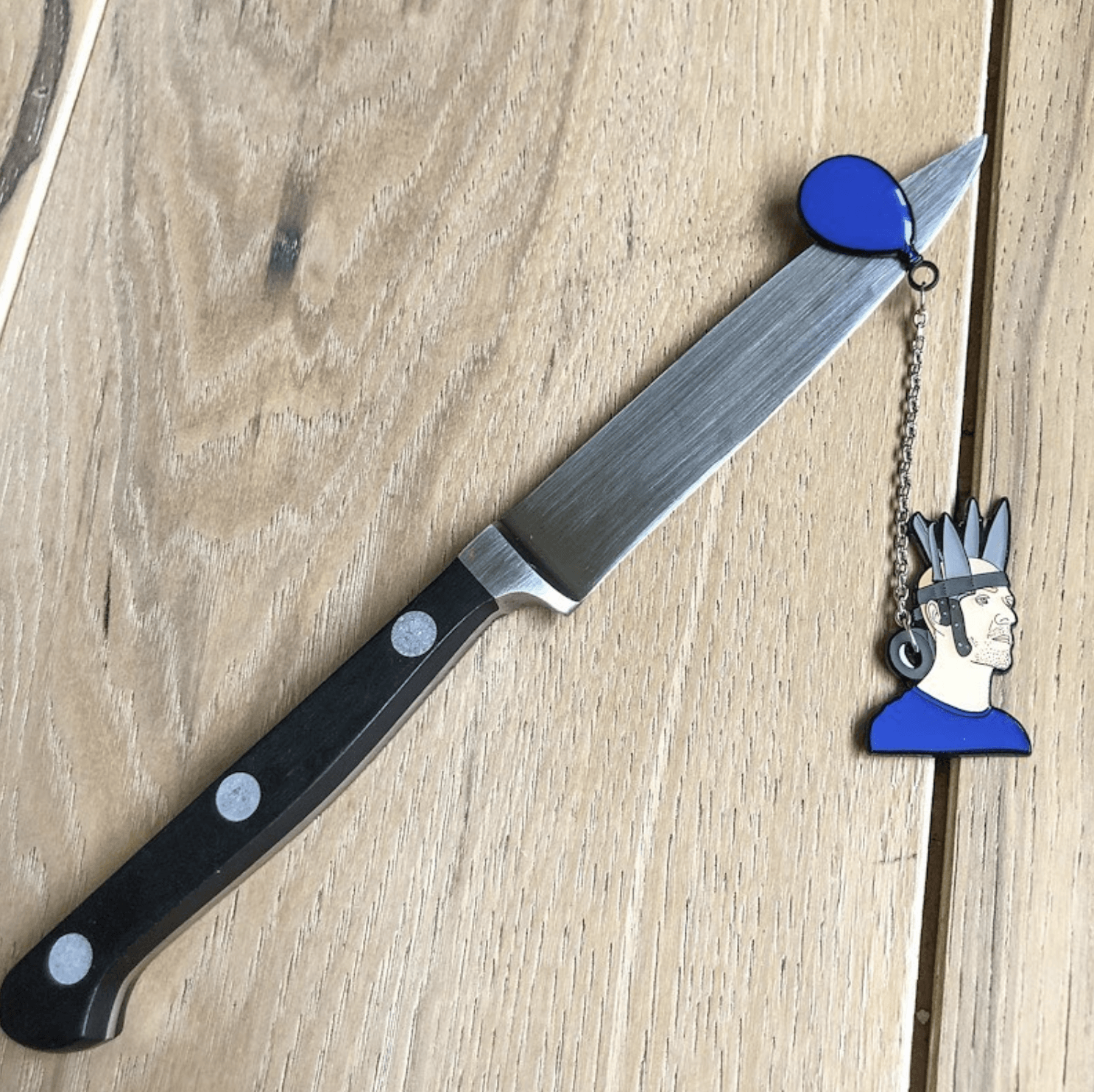 jan hakon erichson enamel pin with Jan wearing a blue shirt and crown of duct taped knives with a blue balloon attatched to a chain goin through the duct tape roll. the balloon of the pin is balanced on a kit hen knife.