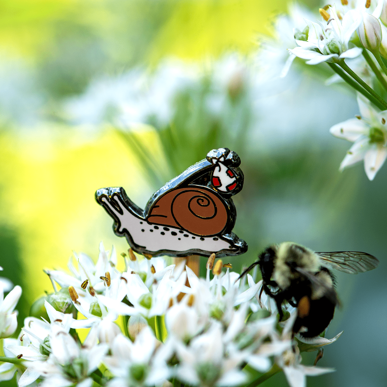 Rover the Snail Mini Pin by The Roving House, featuring a hobo or runaway snail with a bindle exploring garlic flowers alongside a bumblebee.