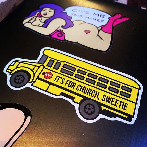 A vinyl sticker on a laptop of a bright yellow schoolbus. The side of the bus reads "IT'S FOR CHURCH, SWEETIE" and it has a red stop sign that says "NEXT!!"