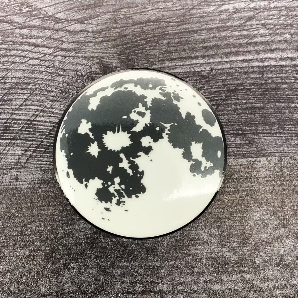 A sticker of the moon in the light. The light flicks off, showing the moon glowing green in the dark, before the light flicks on again.