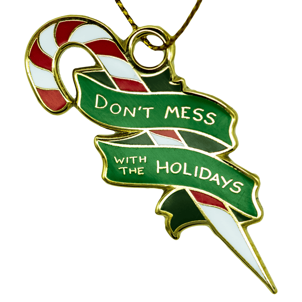 An enamel ornament of a red, white, and silver candy cane sharpened at one end, surrounded by a green banner that reads "DON'T MESS WITH THE HOLIDAYS".