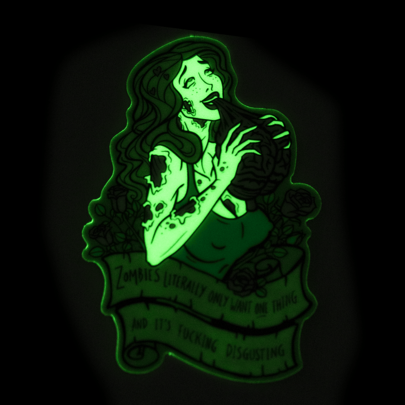 A vinyl sticker glowing green in the dark, featuring the bust of a buxom, attractive female zombie surrounded by roses. She's eating a brain and her eyes are rolled back in her head.