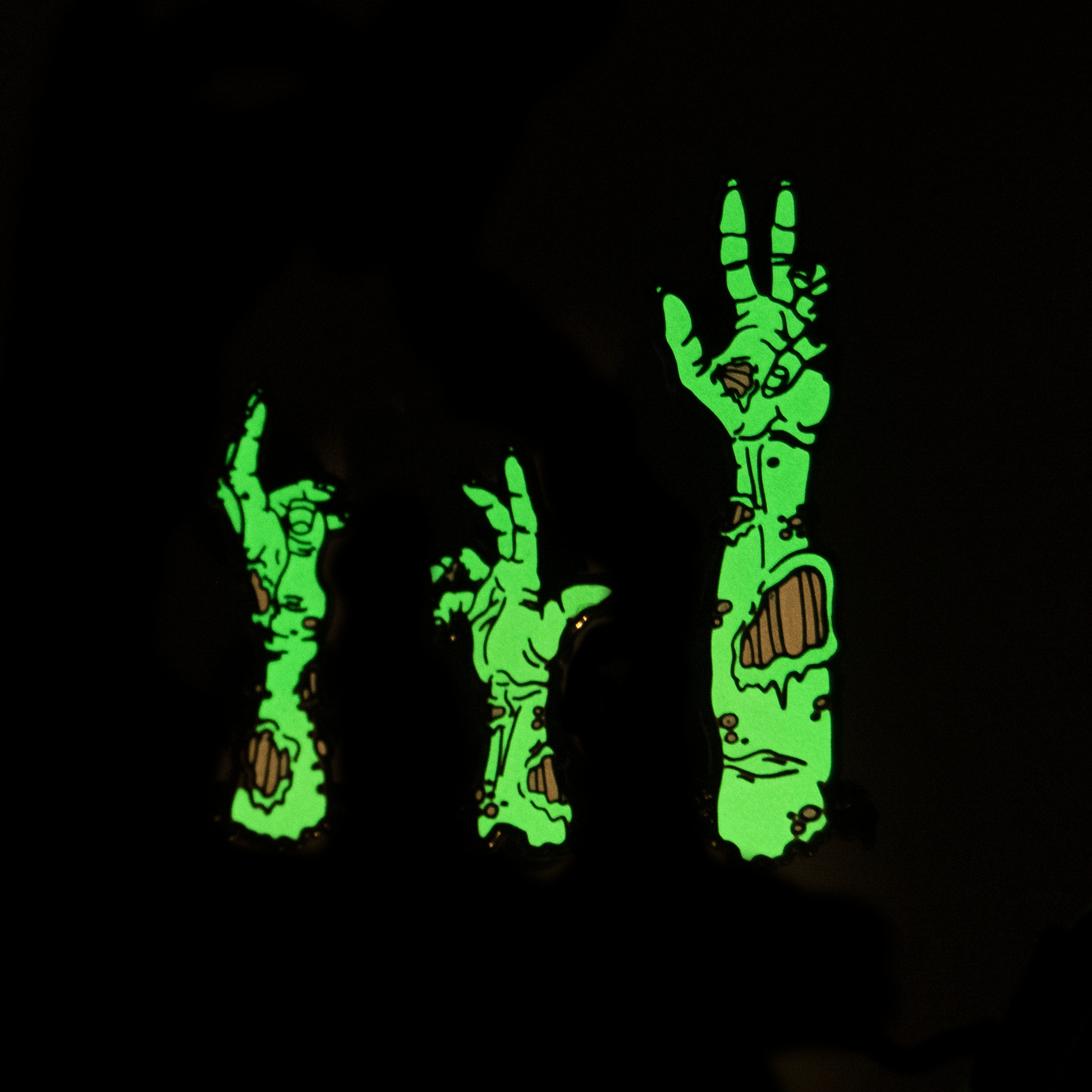 A set of three zombie arm pins, glowing in the dark.