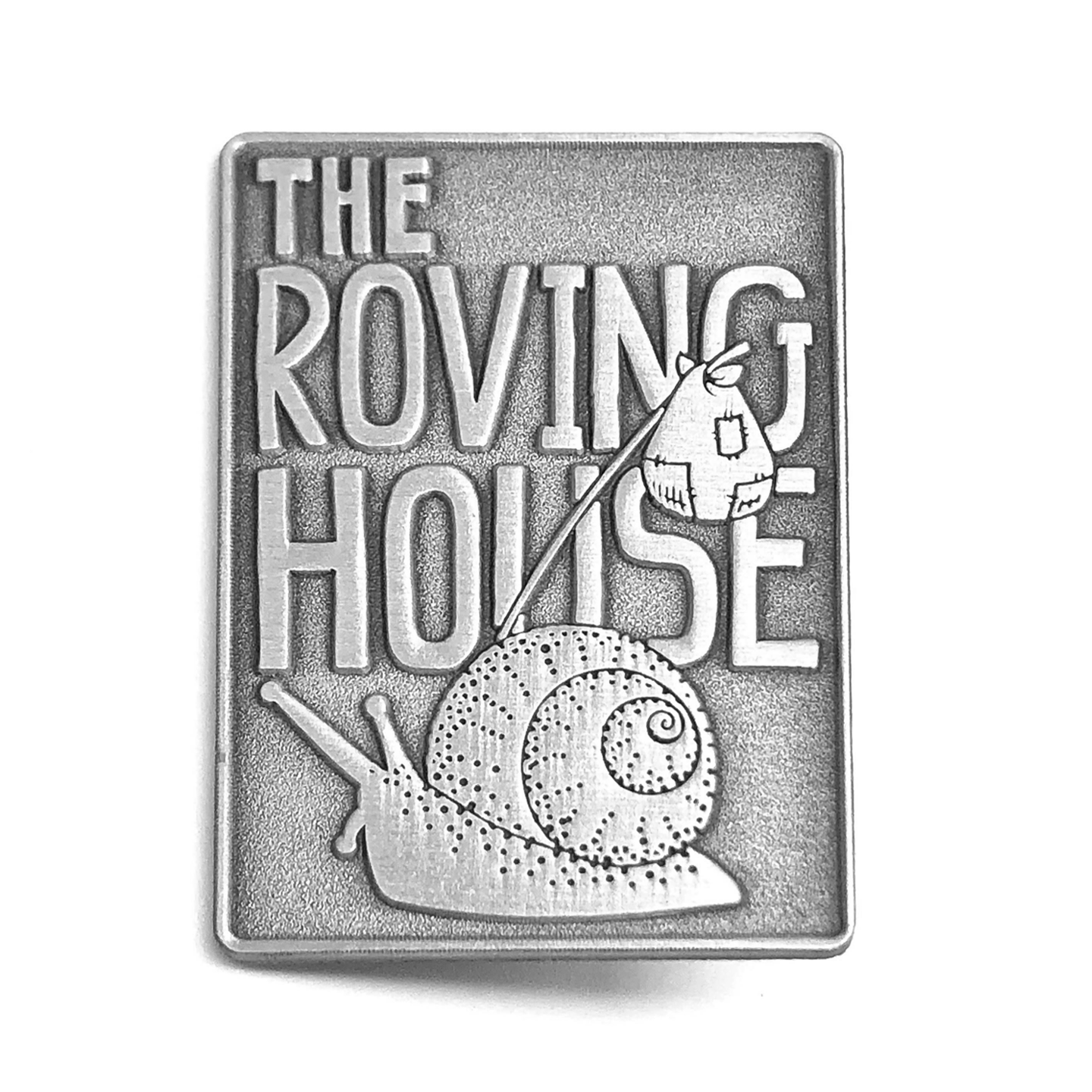A silver, rectangular metal pin of a snail carrying a bindle. Behind him is the text "The Roving House".