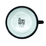 The white inside view of a metal and enamel camp mug. A black and white logo of THE ROVING HOUSE with a snail carrying a bindle is printed on the inside bottom of the mug.